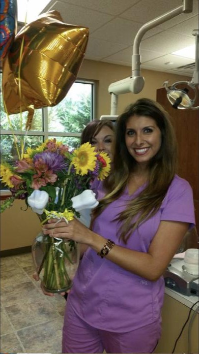 Jessie Boeckmann smiling, holding flowers, in dental office scrubs